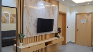 Een modern receptiegedeelte met een grote televisie aan een marmeren wand, een houten console tafel met een telefoon en een potplant.
