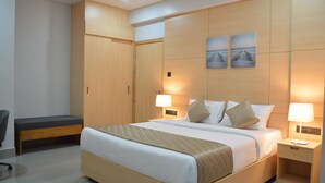 Een hotelkamer met een groot bed, nachtlampjes, een bankje en een kledingkast.
