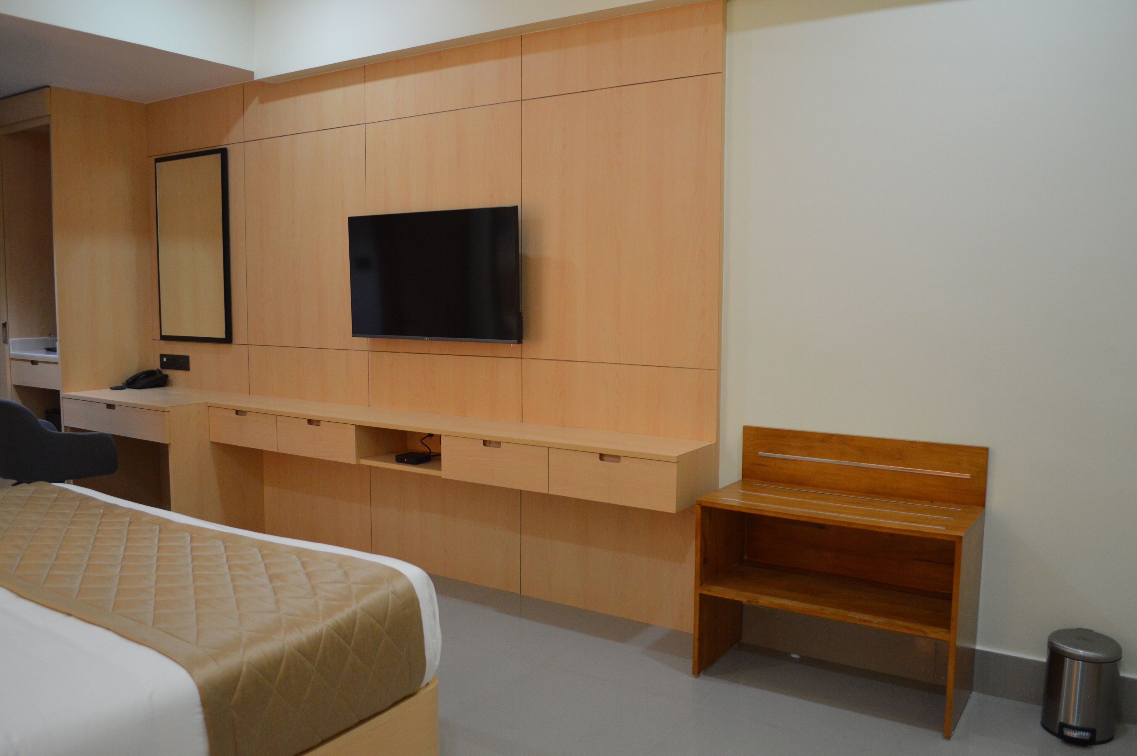 Una camera d'albergo con un letto, una scrivania, un televisore fissato alla parete e una piccola panca in legno.
