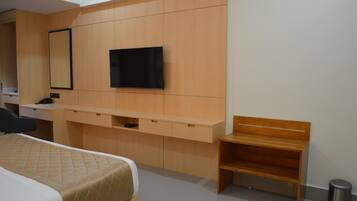 Una camera d'albergo con un letto, una scrivania, un televisore fissato alla parete e una piccola panca in legno.