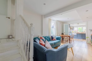 A living room with a sofa, a dining table, and a staircase. - Homely 2BD Flat with Private Garden, North London (Greater London)