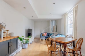 Ein modernes Wohnzimmer mit Essbereich, einer Treppe und einem großen Fenster.