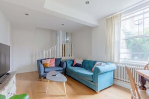 Ein modernes Wohnzimmer mit einer Eckcouch, einem Flachbildfernseher, einem Esstisch und einer Treppe.