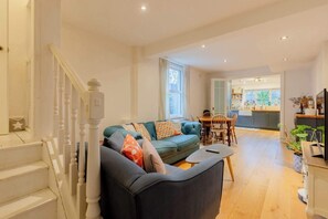 A living room with a sofa, a dining table, and a staircase. - Homely 2BD Flat with Private Garden, North London (Greater London)