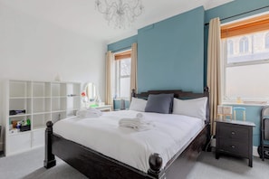 Une chambre bien rangée, avec un lit, des tables de chevet, une armoire et une fenêtre avec des rideaux.