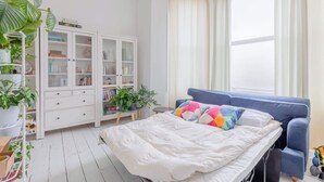 Et soveværelse med seng, blå sofa, hvidt skab og et vindue med gardiner.
