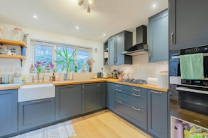A modern kitchen with grey cabinets, a wooden countertop, a window with a view, and a built-in oven. - Homely 2BD Flat with Private Garden, North London (Greater London)