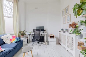 Une pièce avec un canapé bleu, un bureau avec un ordinateur, une armoire blanche et une plante.