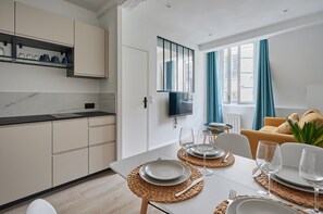 A modern kitchen with white cabinets, a marble countertop, and a dining area set with plates, glasses, and a TV mounted on the wall. - Sublime and new Appartment in Center of Paris (Paris)