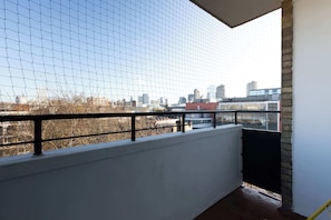 A balcony with a view of a cityscape, a white wall, and a black railing.