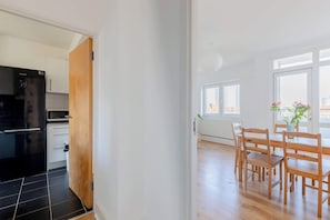 An open door leading to a kitchen with a black refrigerator and a dining area with a wooden table and chairs. - Fantastically Located 4BD Flat, Clerkenwell (Greater London)