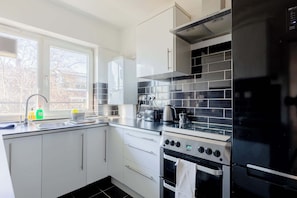 A modern kitchen with white cabinets, a black tiled backsplash, stainless steel appliances, and a window with a view of trees.