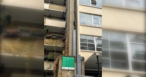 A multi-story building with a green sign indicating flat numbers and corresponding floors. - Fantastically Located 4BD Flat, Clerkenwell (Greater London)