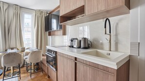 A modern kitchen with wooden cabinets, a white countertop, a built-in oven, and a flat-screen TV mounted above the sink. - New Apartment Center of Paris/le Marais (Paris)