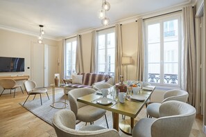A modern hotel room with a dining area, a sofa, and a television. - Sublim new Flat Center of Paris Opera Madeleine (Paris)