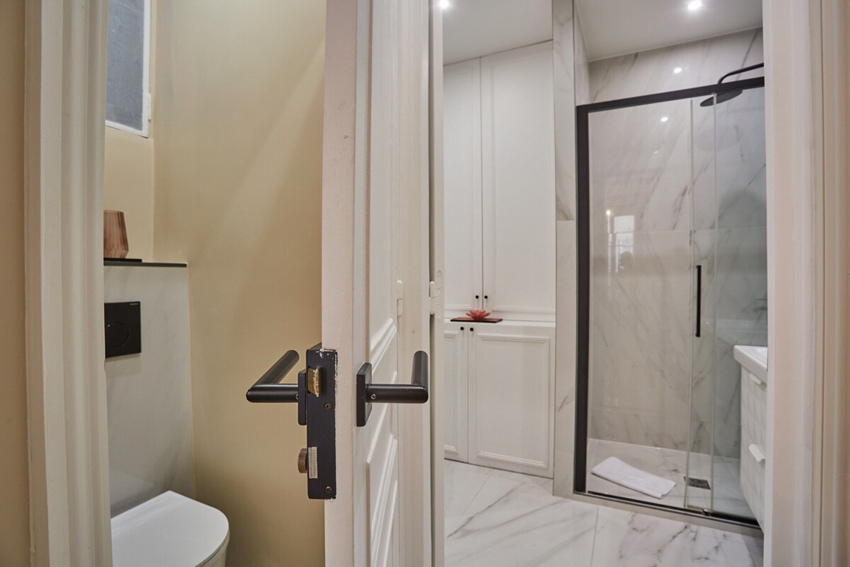 A modern bathroom with a glass-enclosed shower, a white toilet, and a marble floor.