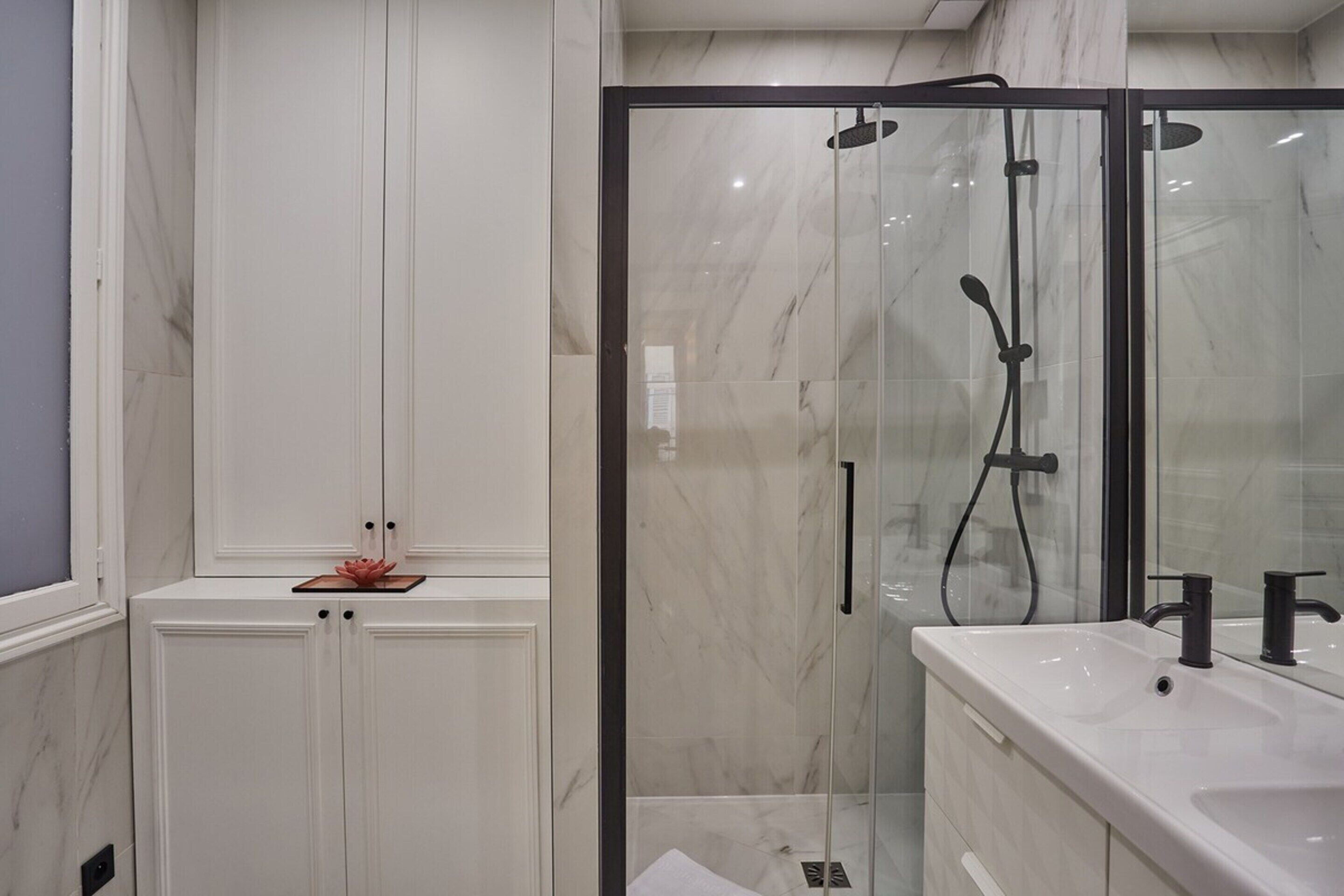 Et moderne badeværelse med et glasafskærmet brusebad, et hvidt toiletbord med vask og marmorvægge.