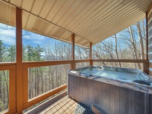 Una terraza de madera con un jacuzzi, rodeada por una barandilla de metal y vistas a un bosque.