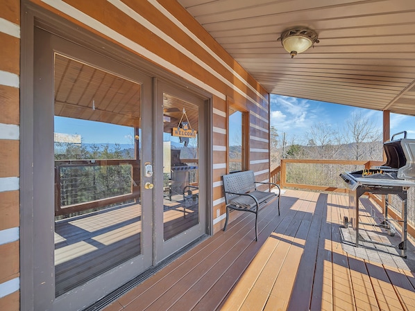 A wooden deck with a grill and a bench, a 'Welcome' sign, and a view of the mountains.