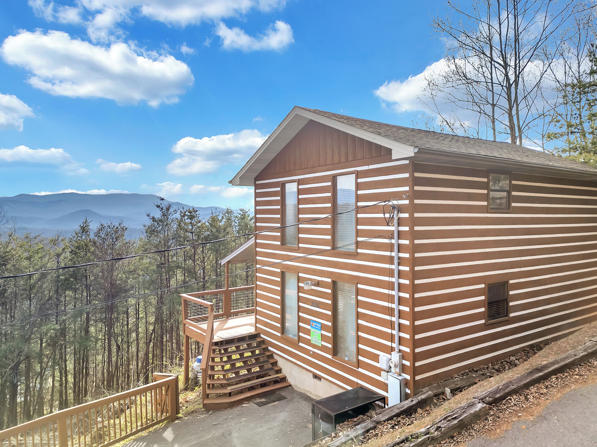 A wooden cabin with a balcony, a staircase, and a view of mountains.