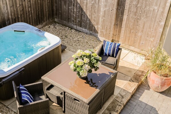Un jacuzzi, muebles de mimbre y una planta en maceta en un patio trasero.