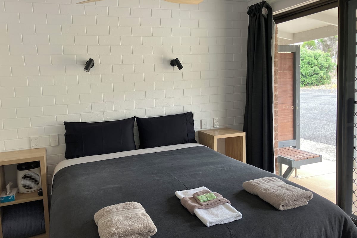 Een moderne slaapkamer met een groot bed, twee nachtkastjes, een plafondventilator en uitzicht op de omgeving.