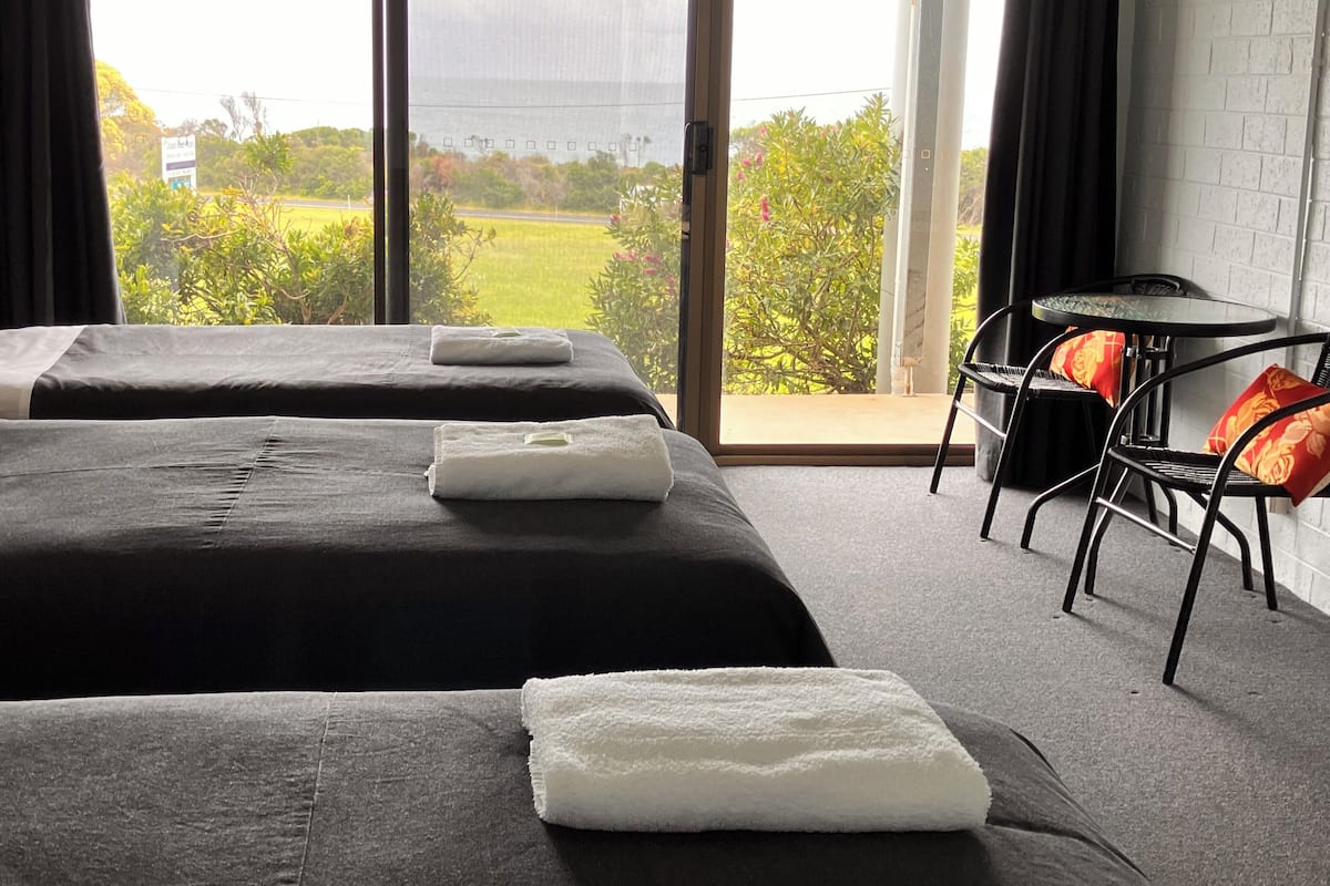 Hotelkamer met twee bedden, een tafeltje en uitzicht op groen en een weg.