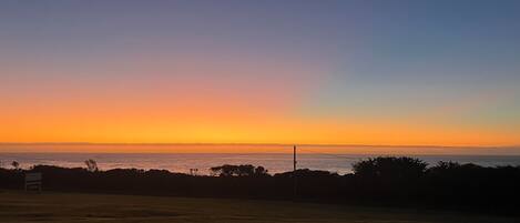 A sunset over a grassy field with a view of the ocean.