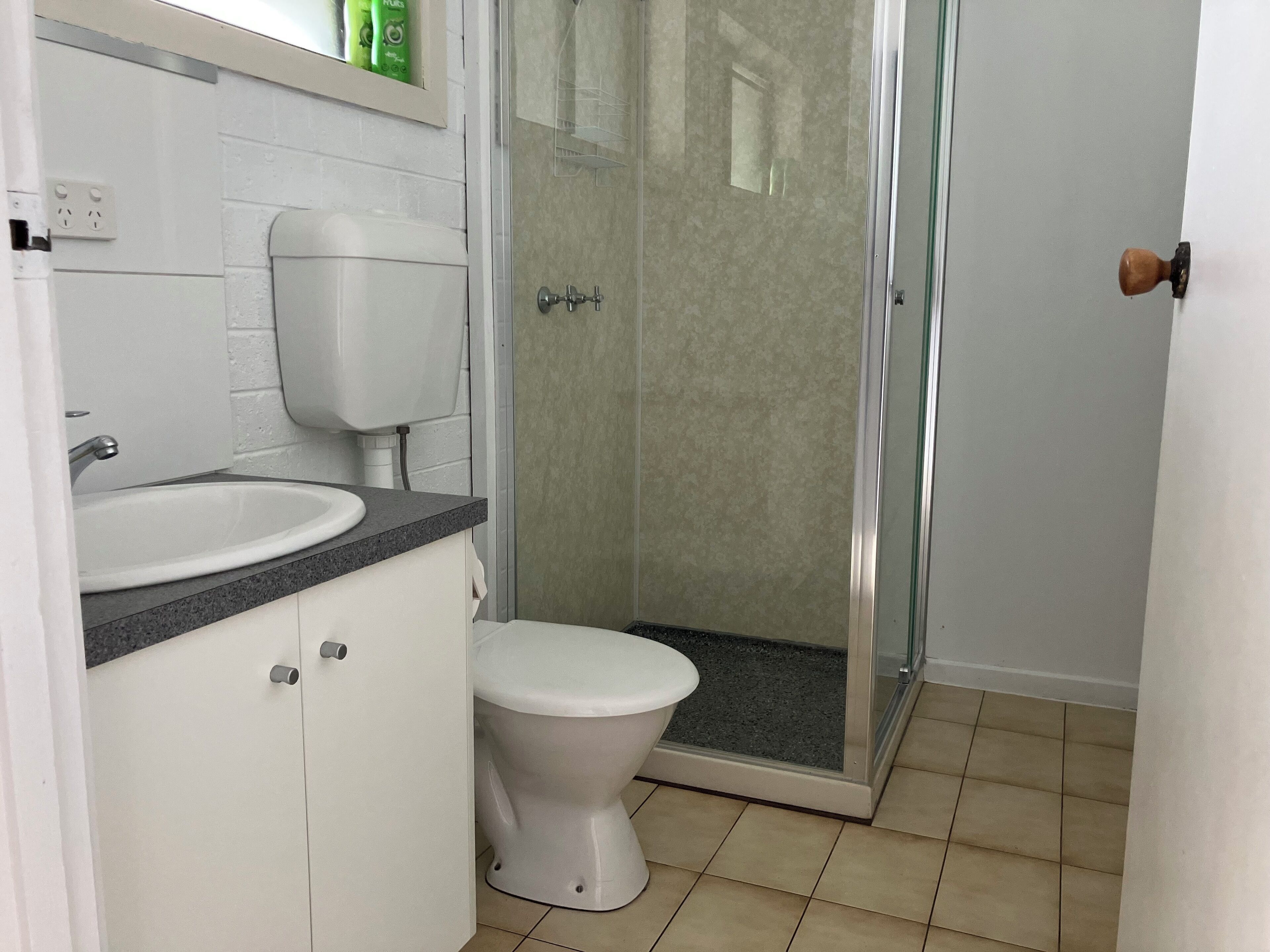 Une salle de bain avec des toilettes blanches, un lavabo doté d’un plan de travail en granit et un espace douche.