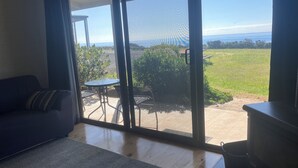 A room with a sliding glass door leading to an outdoor patio with a table and chairs. - 61 OCEAN ROAD MOTEL  (Skenes Creek)