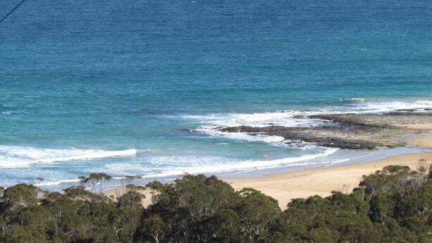 A coastal landscape with a sandy beach, rocky outcrops, and dense green foliage. - 61 OCEAN ROAD MOTEL  (Skenes Creek)