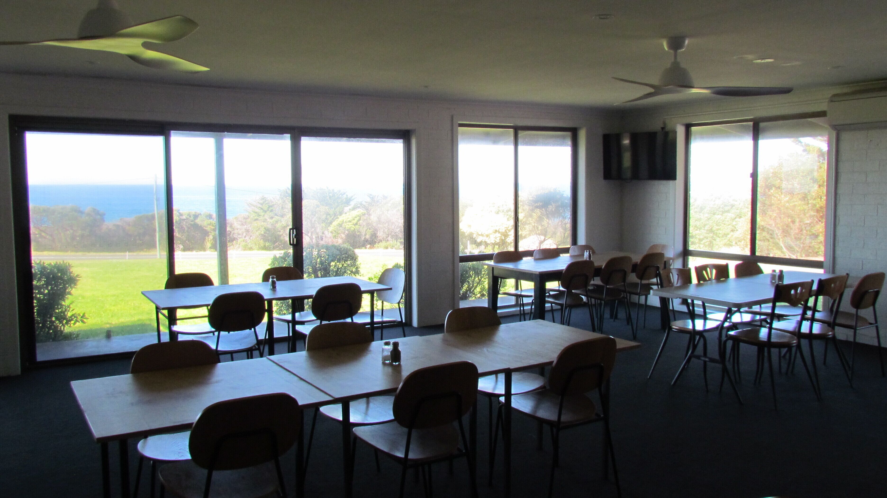 A conference room with tables and chairs, large windows with a view of the outdoors, and ceiling fans.