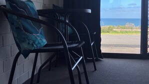 A room with a view of the ocean, featuring a brick wall, a black metal bench, and a dark curtain. - 61 OCEAN ROAD MOTEL  (Skenes Creek)