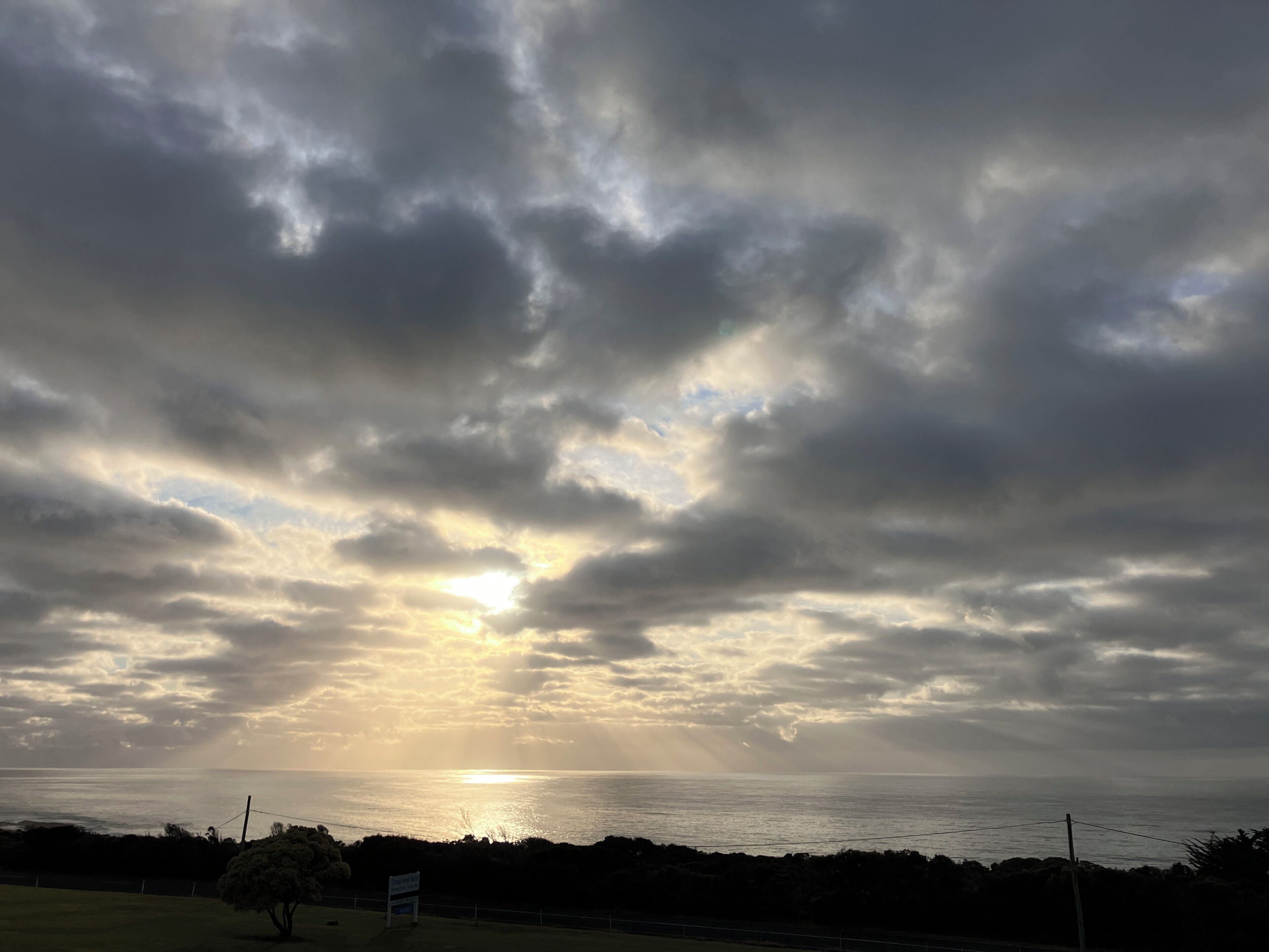 A coastal landscape with a cloudy sky and the sun setting or rising over the ocean.