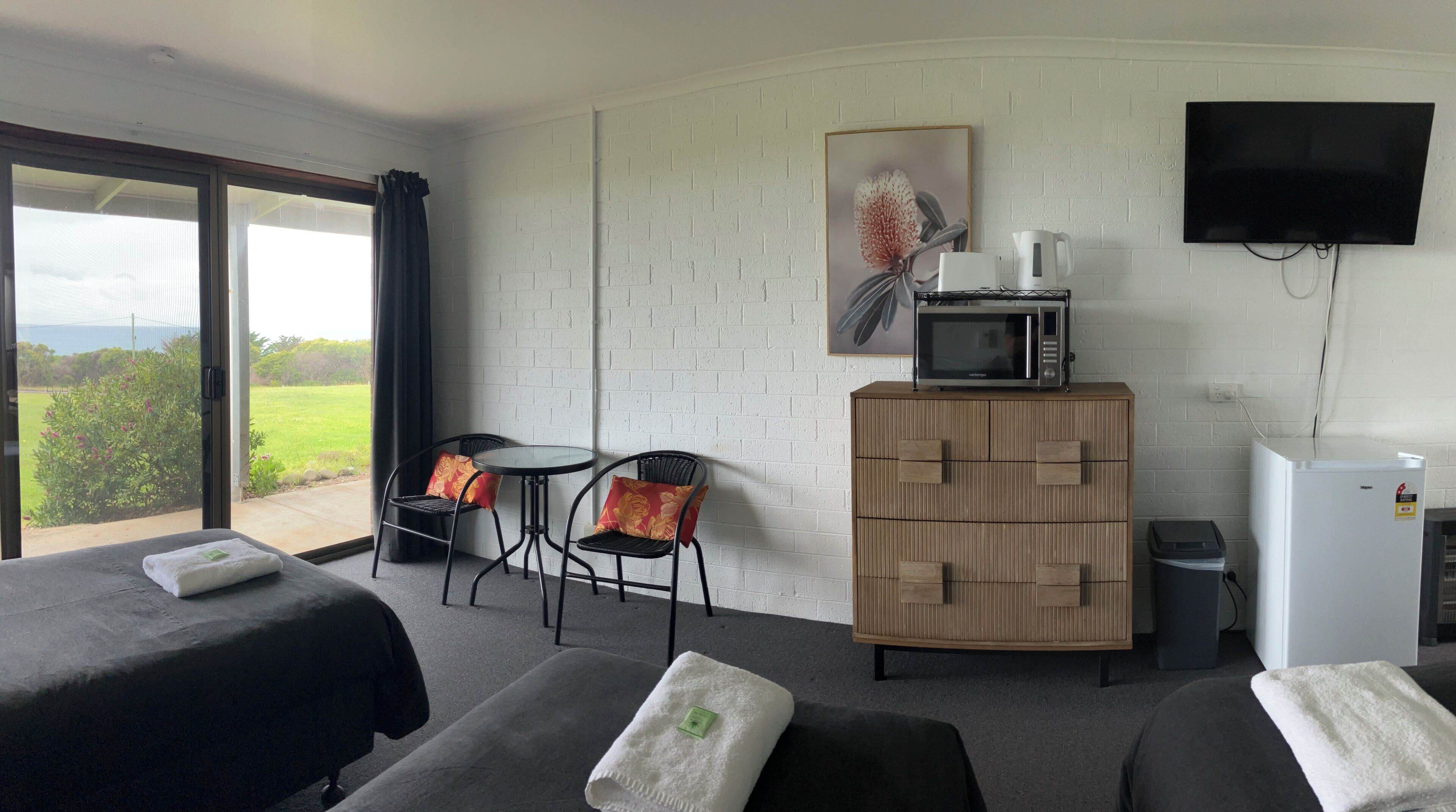 A hotel room with two beds, a small table with chairs, a microwave, a TV, and a view of the outdoors.