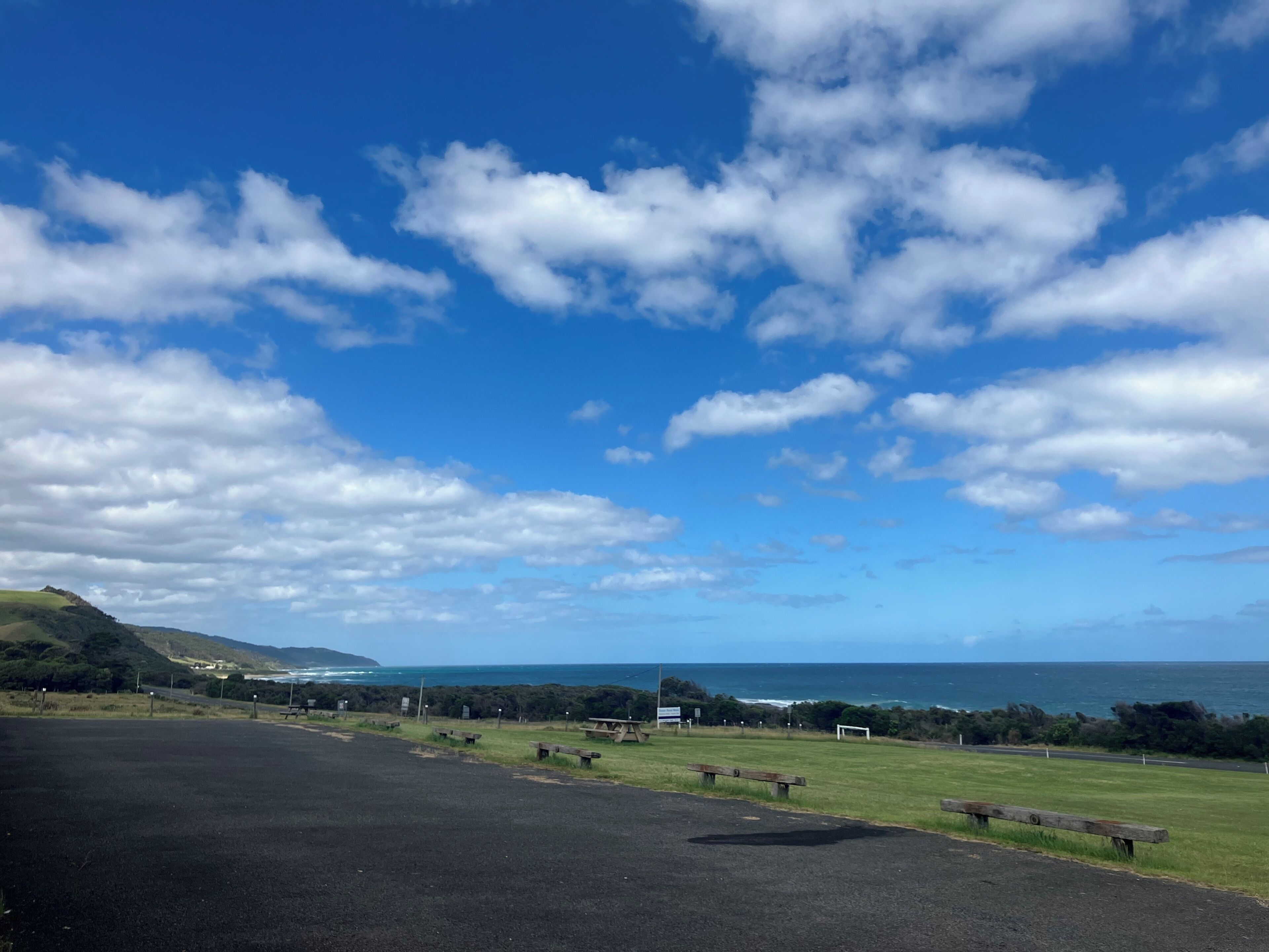 A coastal road with picnic benches and a grassy area.