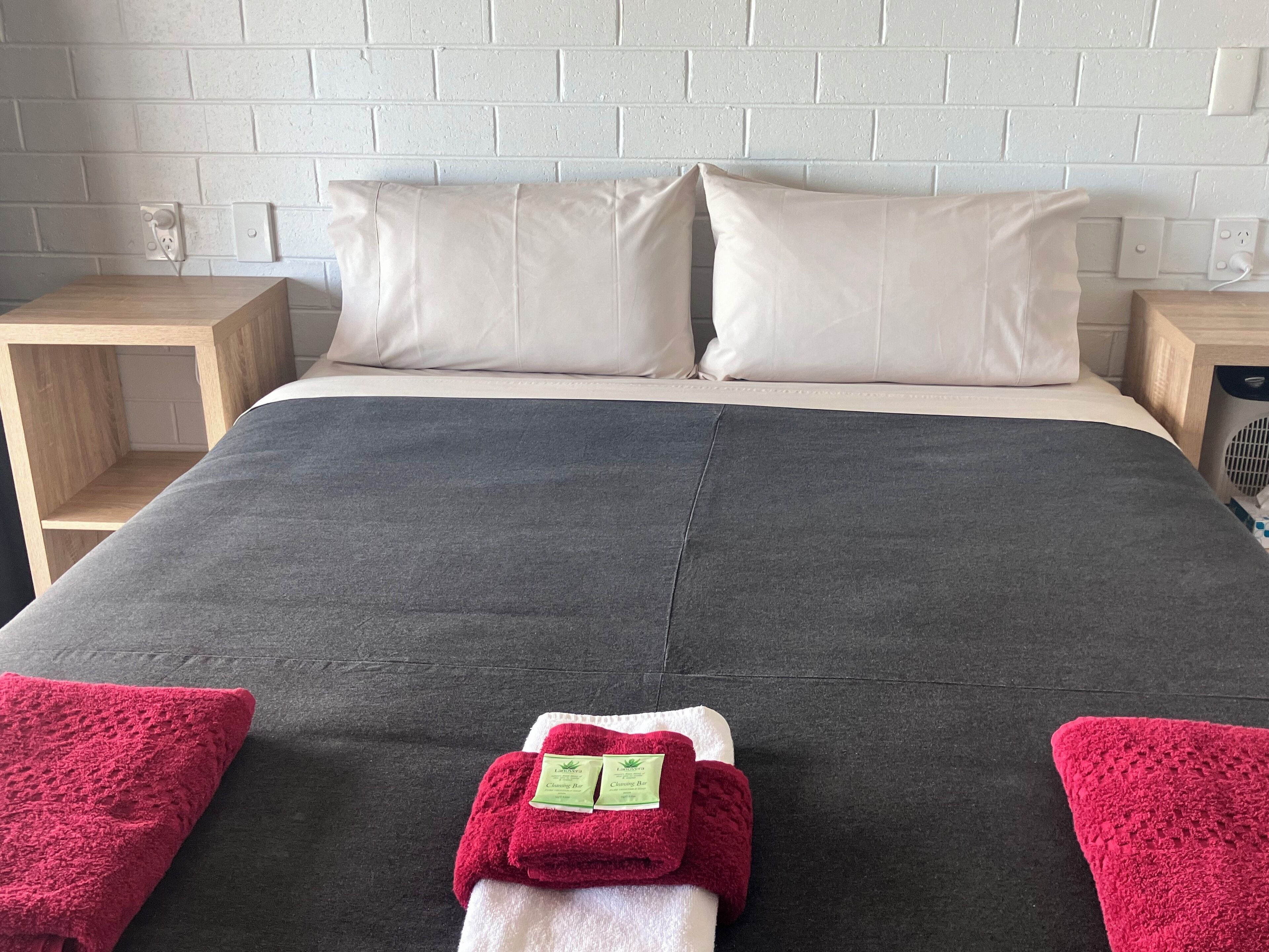A neatly made bed with a grey bedspread, two white pillows, and two red towels on either side.