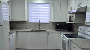 A modern kitchen with white cabinets, a stainless steel microwave, a built-in oven, and a window with blinds. - Large, luxurious apartment in Ville Saint-Laurent  (Montréal)