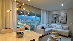 Una sala de estar moderna con comedor, un conjunto de sofás y un amplio ventanal con vista a la ciudad.