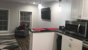 Una cocina compacta con microondas, una pequeña isla con individuales rojos y un televisor de pantalla plana montado en la pared.