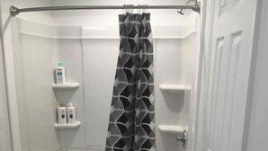 Una ducha con cortina de baño blanco y negro estampada, una bañera blanca y un estante pequeño con artículos de aseo.