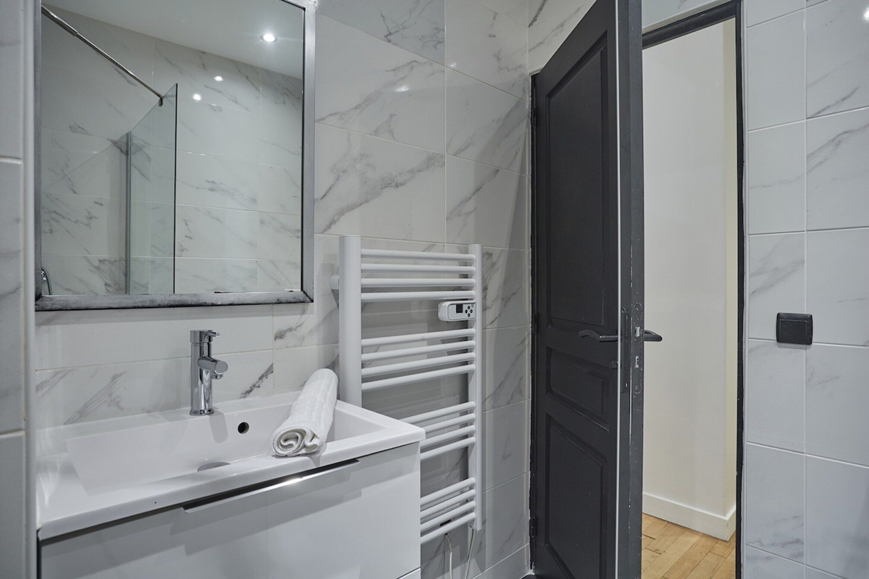 A modern bathroom with a white sink, a mirror, and a towel rack.