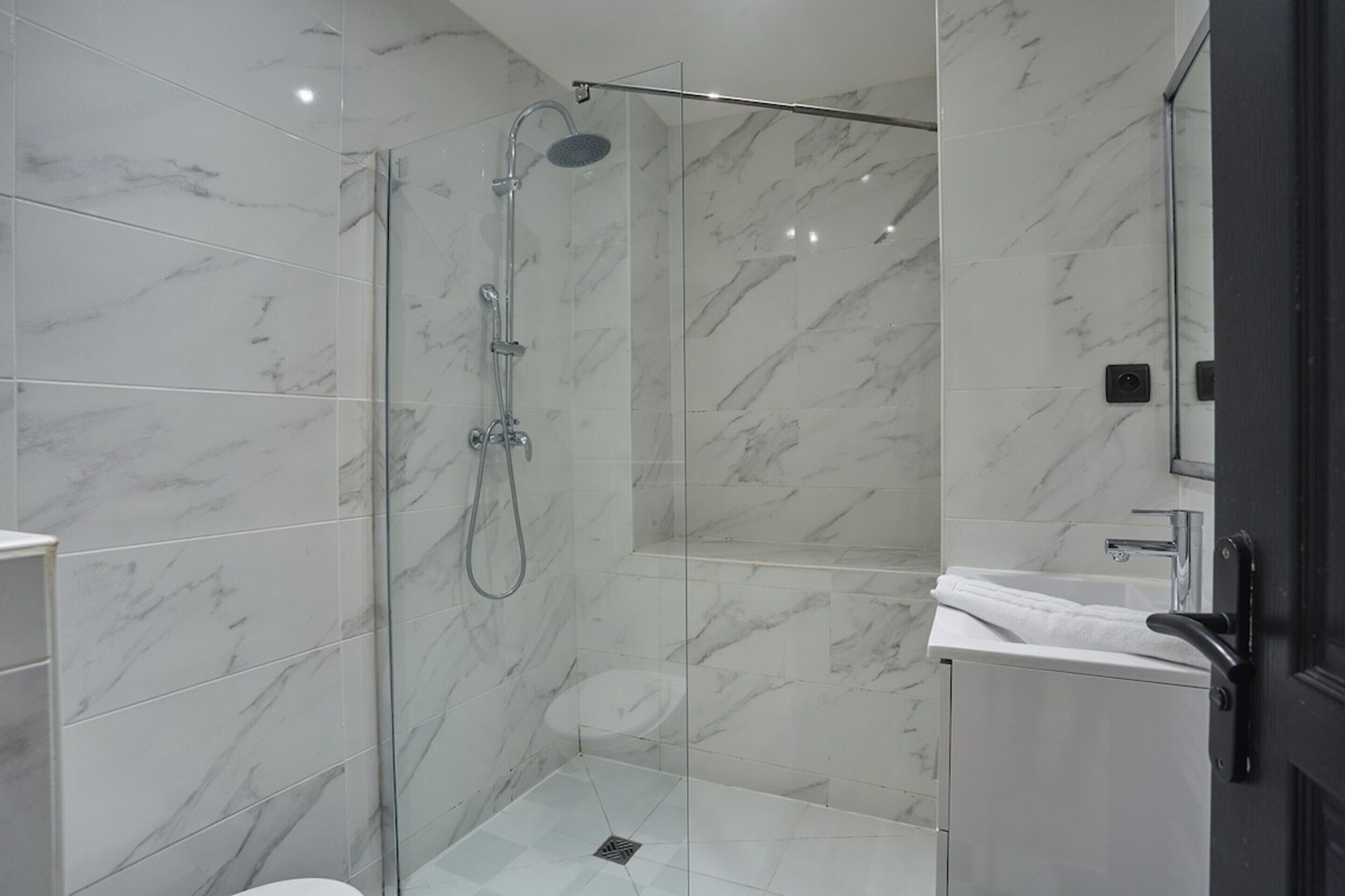 A modern bathroom with a glass-enclosed shower, a white sink, and a marble-tiled wall.
