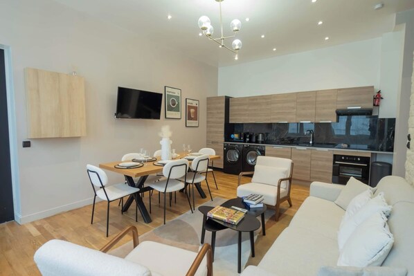 A modern living room with a sofa, coffee table, and dining area with chairs. A kitchen with appliances and wooden cabinets is visible in the background. - Spacious Air-conditioned Apartment Center of Paris (Paris)
