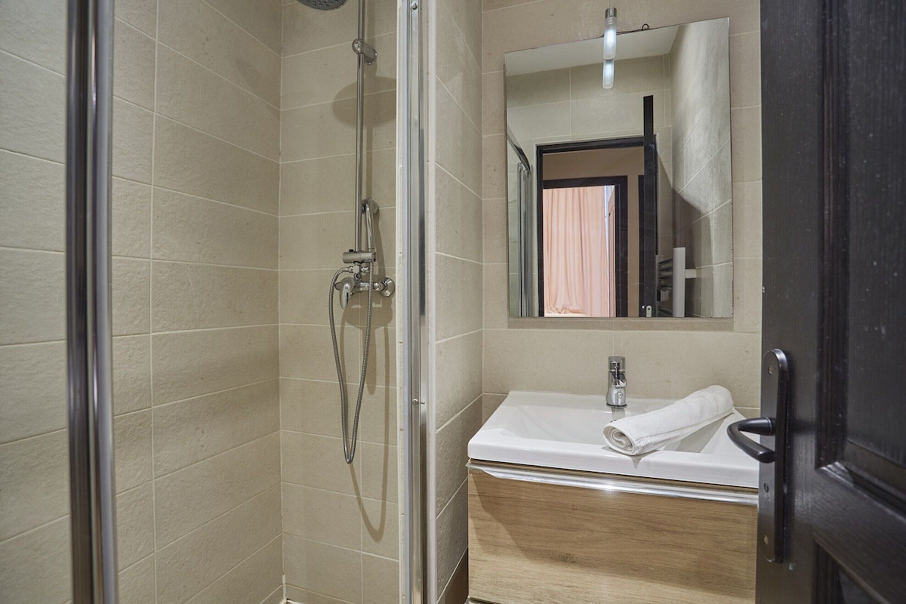 A bathroom with a glass shower enclosure, a sink with a wooden cabinet, and a mirror with a towel on the counter.