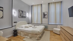Ένα σύγχρονο υπνοδωμάτιο με κρεβάτι, κομοδίνα, μια καρέκλα, μια συρταριέρα και έργα τέχνης στους τοίχους.