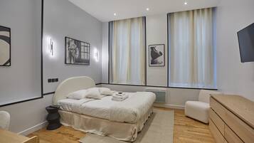 A modern bedroom with a bed, bedside tables, a chair, a dresser, and artwork on the walls.