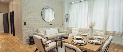 A modern dining area with a wooden table set for four, surrounded by chairs, in a room with a stone wall and a large mirror.