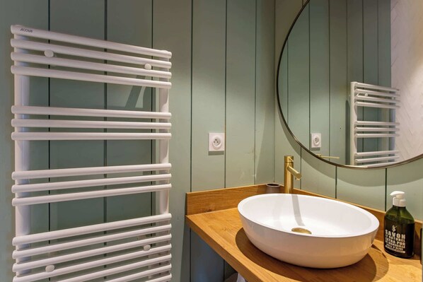 Un baño con un radiador blanco, un espejo redondo y una encimera de madera con un lavabo blanco y una botella de jabón.
