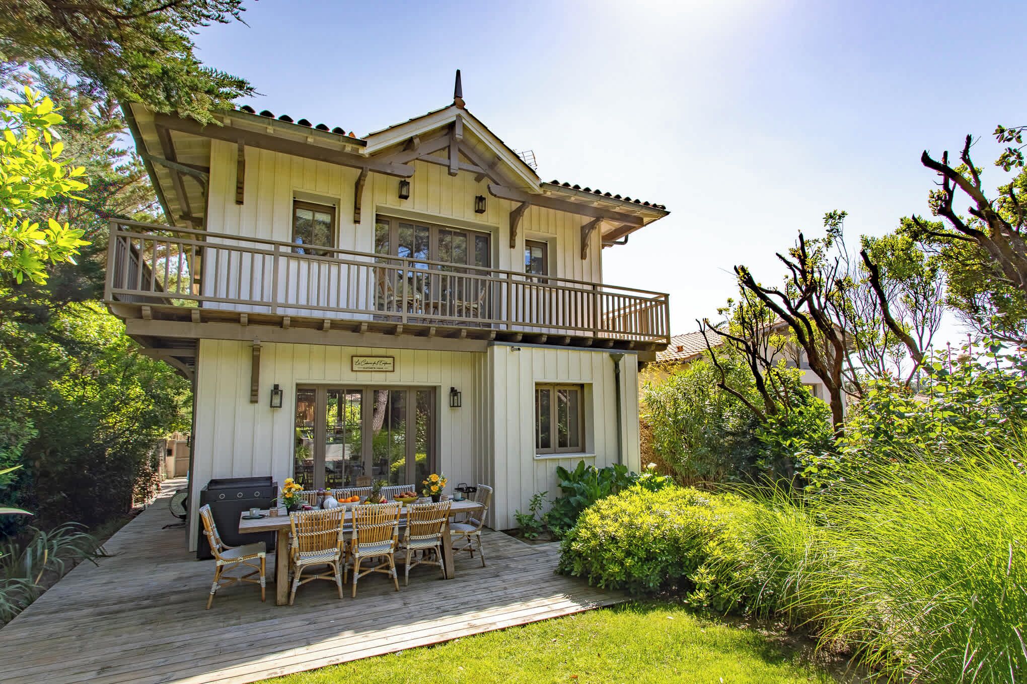 A two-story house with a balcony, a deck with outdoor furniture, and a garden.